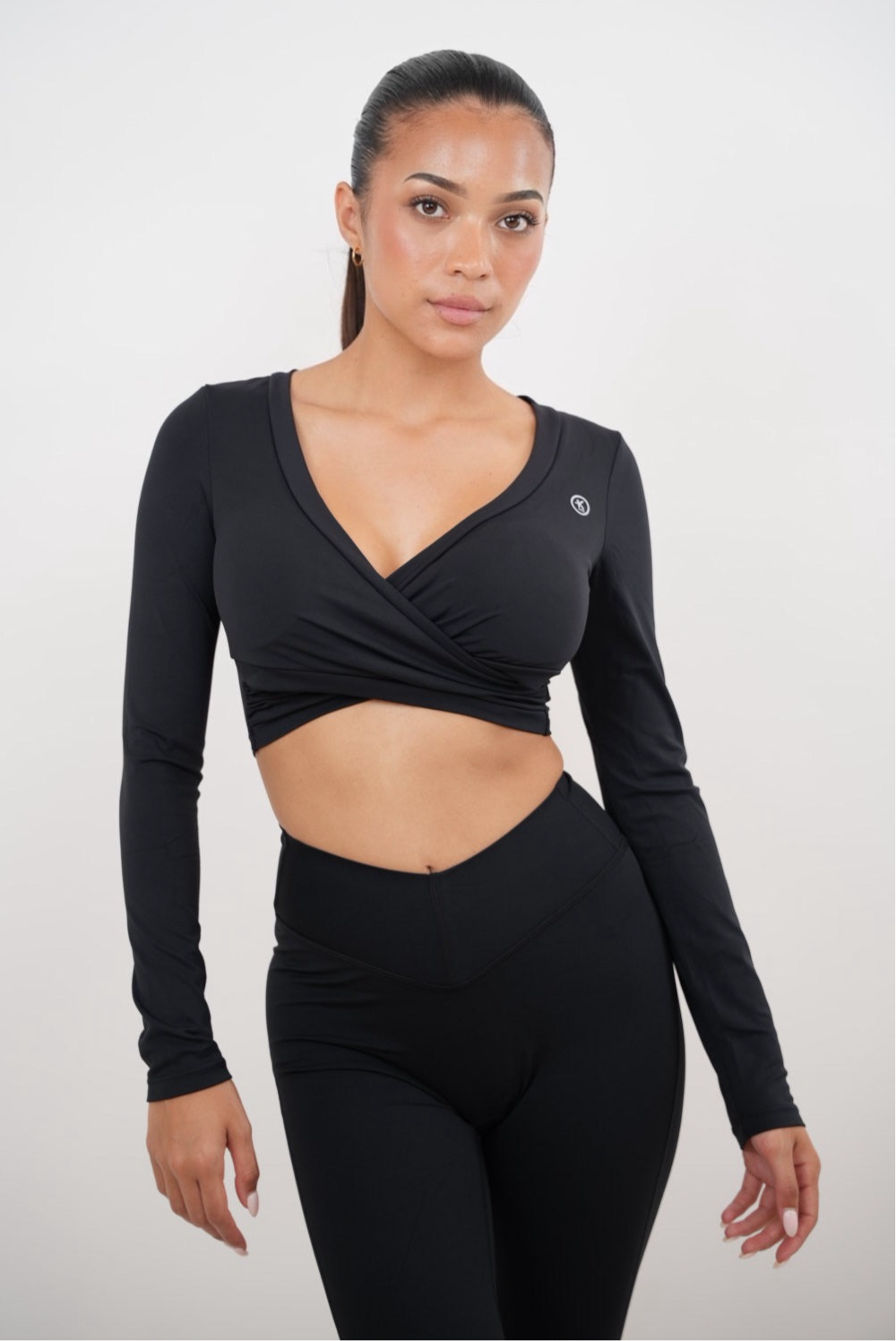 Woman wearing a black long-sleeve crop top and leggings on a white background