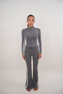 Woman wearing a gray athletic outfit with white stripes on a white background
